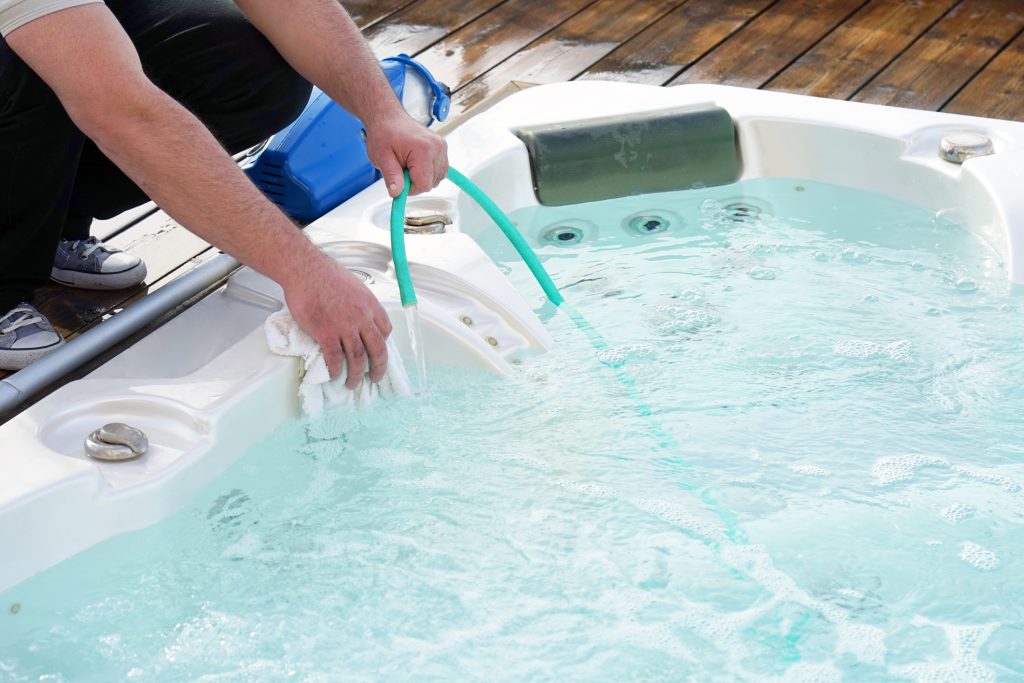 Filling Hot Tub Image of a man bending over a hot tub filling it with hose water.