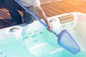 Man straining hot tub Image of a man bending over a hot tub using a strainer to get organic matter out of the spa.