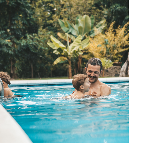 Father and Son Swimming Father and young son swimming in an outdoor pool with greenery surrounding it.