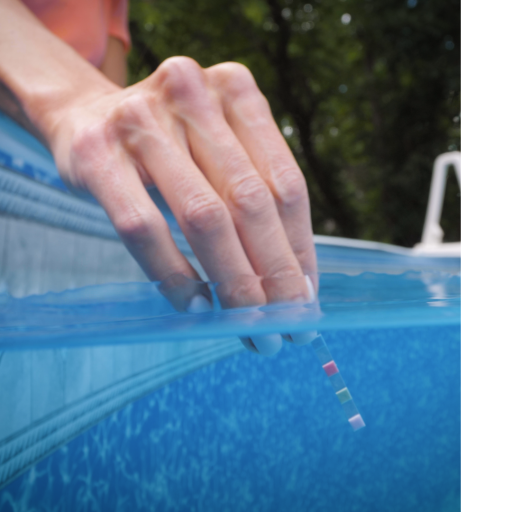 A hand reaches over a soft-sided pool to dip a test strip in the water.