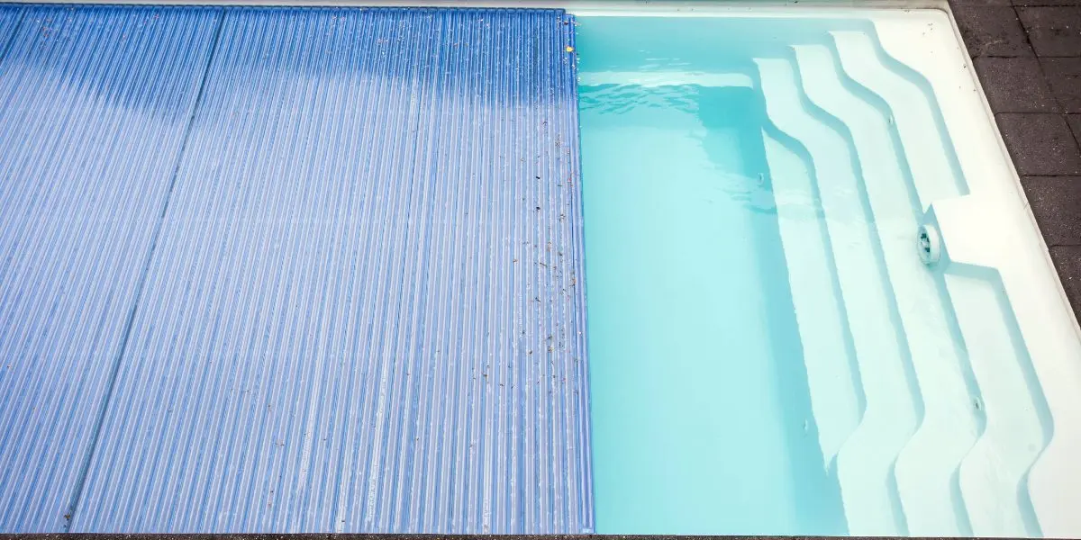A pool cover being pulled over an outdoor pool
