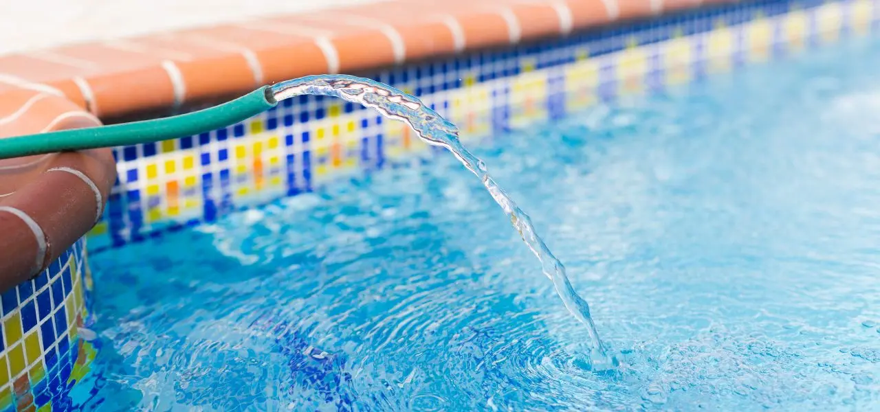 A green hose hangs over the side of a patterned underground pool, filling it with water.