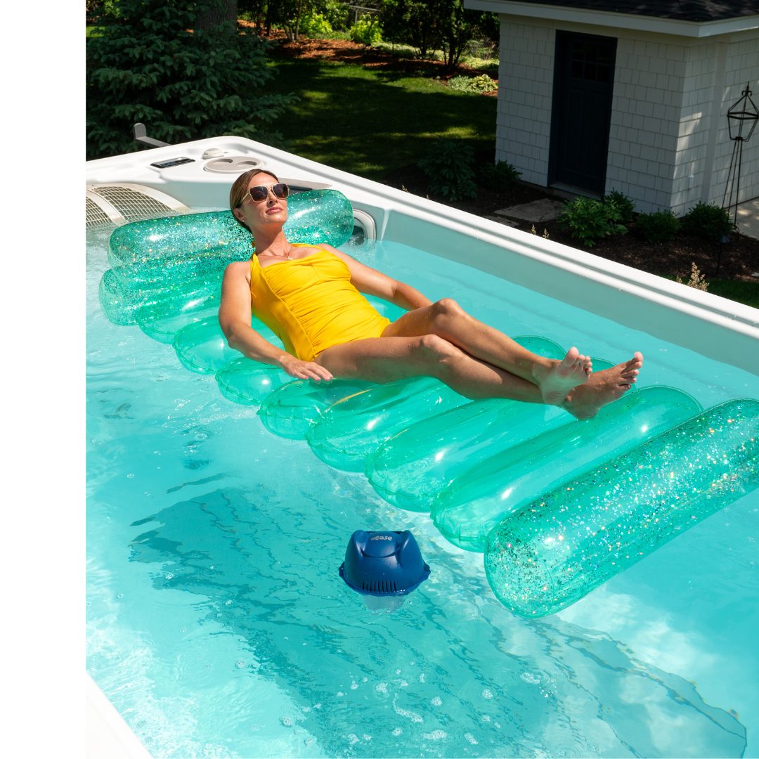 A woman in a yellow swimsuit relaxes in her swim spa on a clear floatation device!