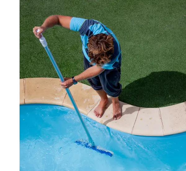 A man stands on the edge of a pool barefoot skimming the side of the pool underwater.