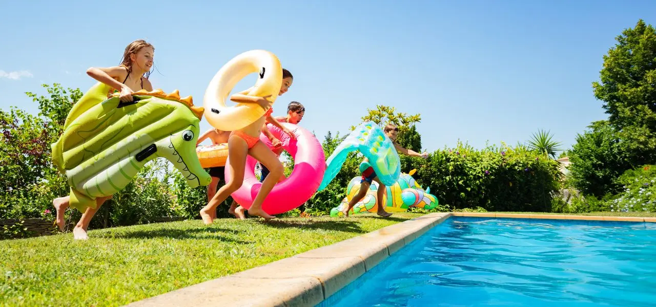 A group of kids holding pool floaties running into the pool