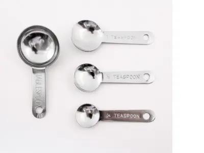 Various silver measuring spoons sit on a grey background