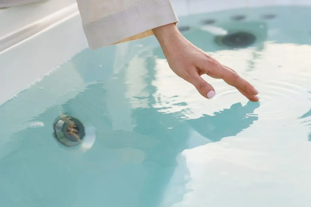 A woman's hand reaches and skims the surface of a clear hot tub's water