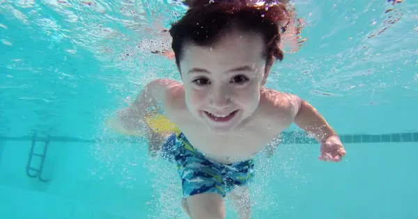 Child smiling underwater with eyes open in a clear swimming pool.