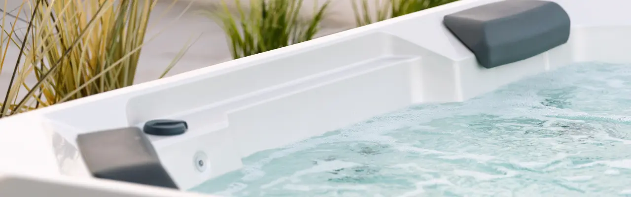 A wide camera shot of an outdoor hot tub with greenery behind it.
