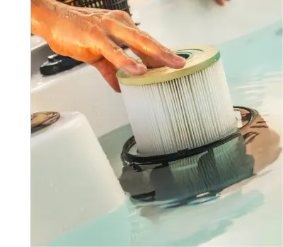 A man's hands pull an old hot tub filter out of the hot tub.