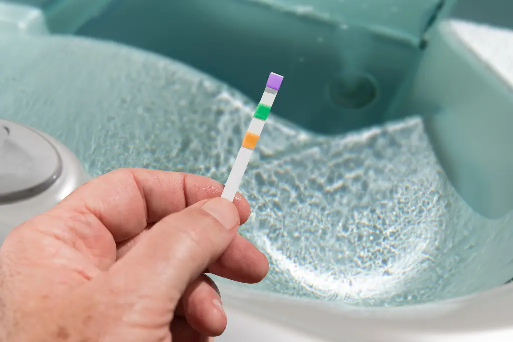 A female's hand dips a test strip into a hot tub.