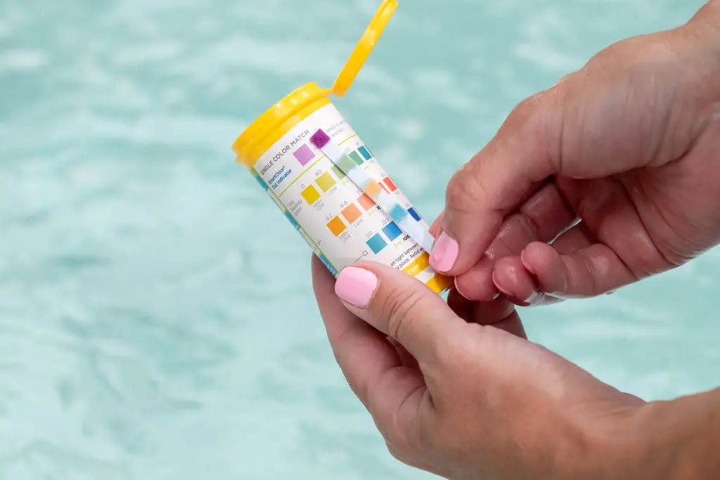 A woman with pink nail polish tests her swim spa with FROG @ease Test Strips