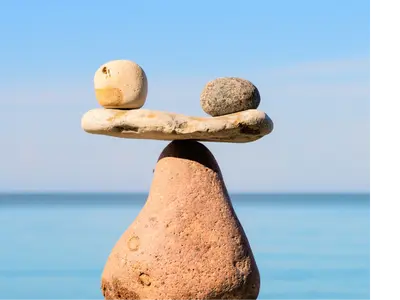 A scale built out of grey stones. the scale is balanced at 180 degrees. In the background is water and rolling hills.