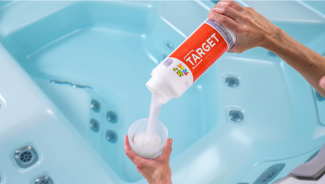 FROG® @ease® Target being poured into a TruDose™ cap above a crystal clear hot tub — precise, easy sanitizer dosing.
