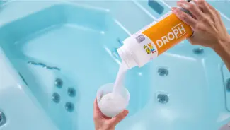 FROG® DropH® being poured into a TruDose™ cap above a hot tub for precise pH and alkalinity adjustment.